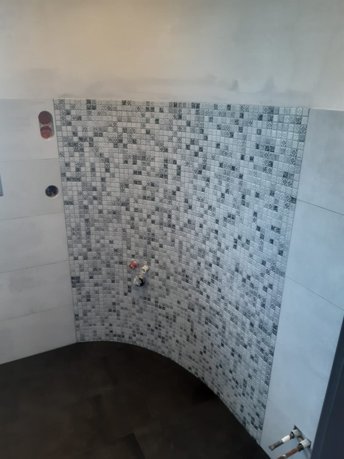 Gerundete Duschwand mit Mosaikfliesen in Grautönen
